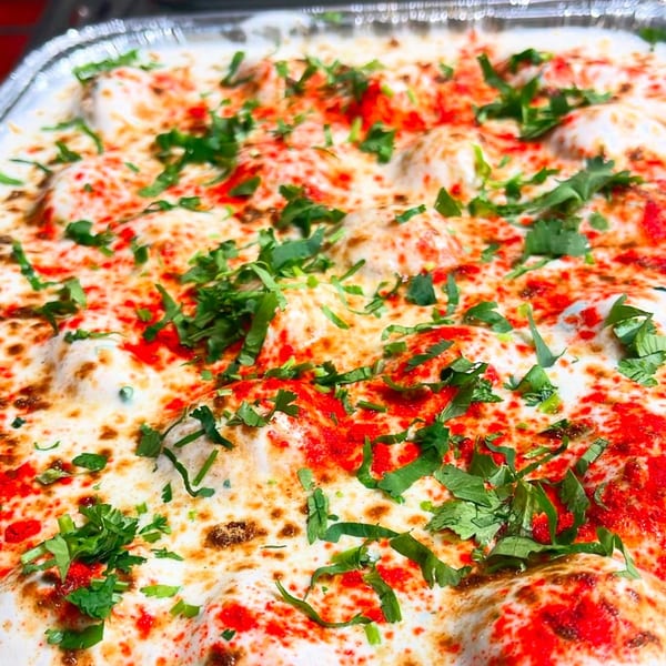 Close-up of Indian Dahi Bhalla, a yogurt-based dish, garnished with red spices and fresh green herbs.