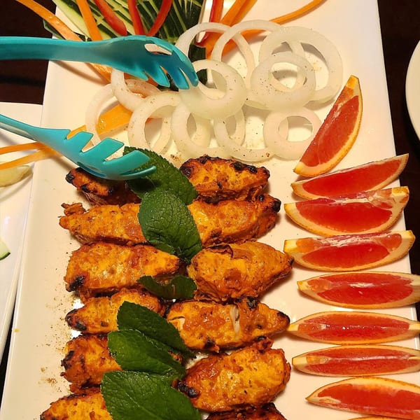 Indian chicken tikka with mint, onion rings, and grapefruit slices on a white platter.