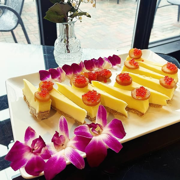 Slices of cheesecake with red caviar-like topping and purple orchid garnishes on a white platter.