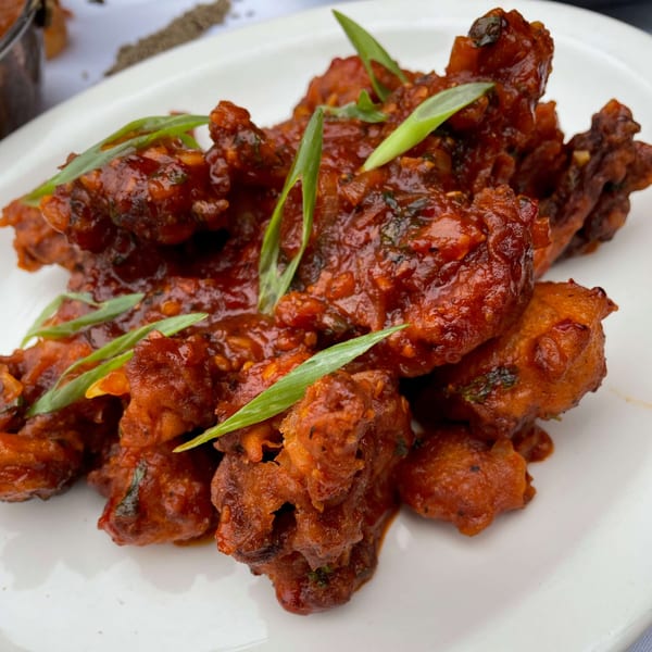 Dear Delhi's Indian chili chicken, coated in a rich red sauce and garnished with fresh green onions.