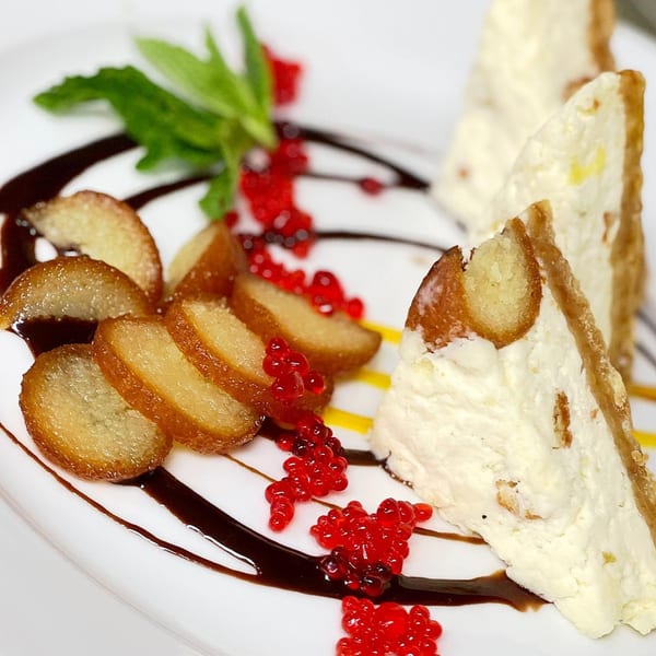 Indian dessert with white cake slices, fried banana, red berries, and chocolate drizzle on a white plate.