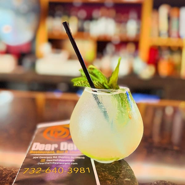 A refreshing cocktail with mint and a straw sits on a Dear Delhi menu at the bar.