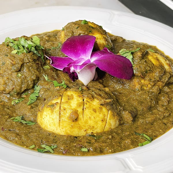 Dear Delhi's egg curry, featuring hard-boiled eggs in a rich green sauce, garnished with cilantro and an orchid.