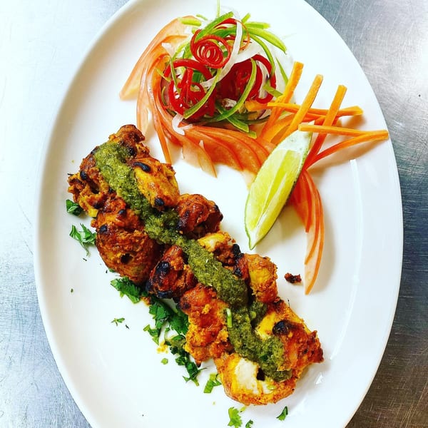 Indian chicken tikka with green chutney, fresh herbs, and a side salad with lime.