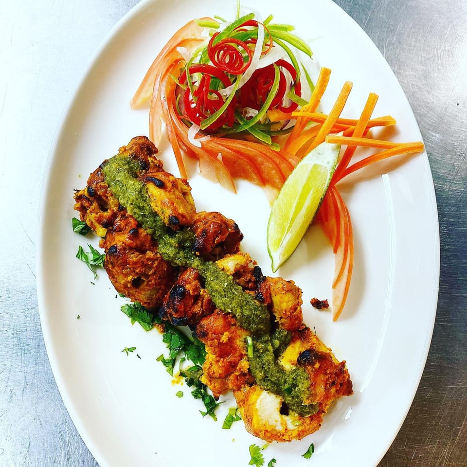 Indian chicken tikka with green chutney, fresh herbs, and a side salad with lime.